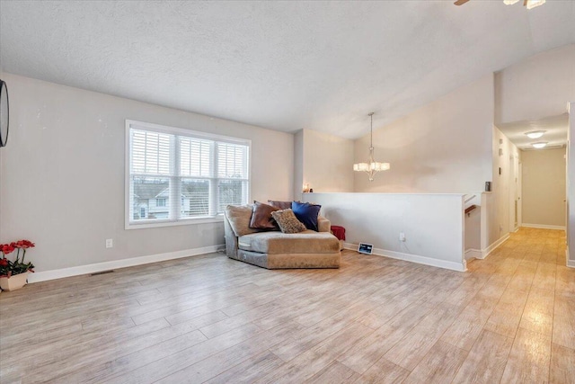 living area with a textured ceiling, light wood-type flooring, vaulted ceiling, and ceiling fan with notable chandelier