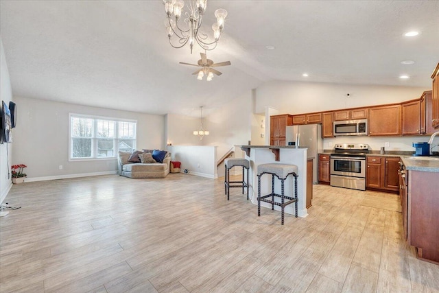 kitchen with a kitchen island, light wood-type flooring, a breakfast bar area, ceiling fan with notable chandelier, and appliances with stainless steel finishes