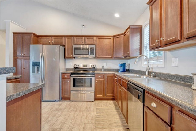 kitchen with appliances with stainless steel finishes, light wood-type flooring, lofted ceiling, and sink