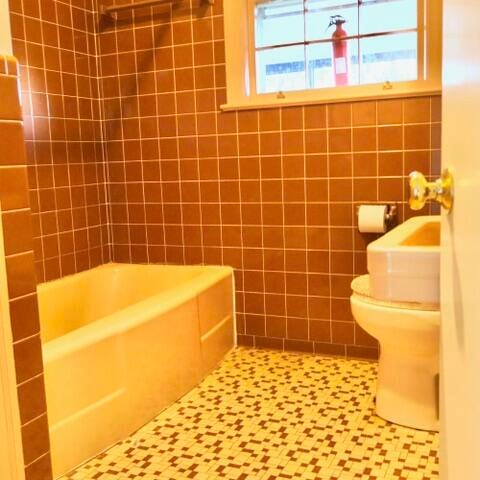 bathroom with tile walls, tiled shower / bath combo, toilet, and tile patterned flooring