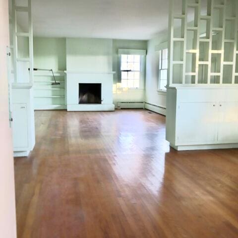 unfurnished living room with a baseboard heating unit and wood-type flooring