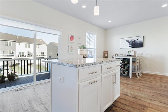 kitchen with white cabinets, light wood-type flooring, a center island, pendant lighting, and light stone counters