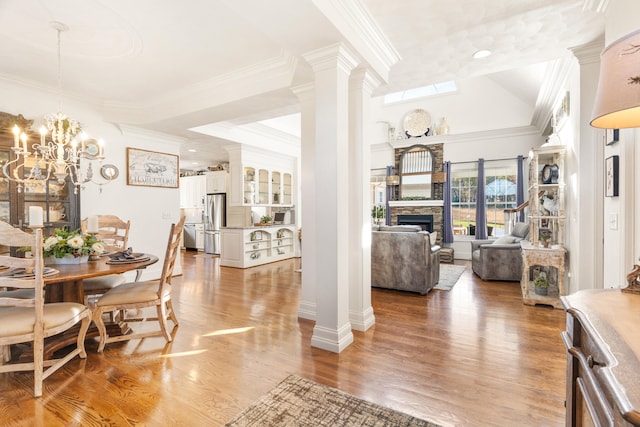 dining space with crown molding, a stone fireplace, an inviting chandelier, and hardwood / wood-style floors