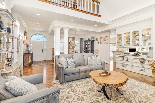 living room with ornate columns, light hardwood / wood-style floors, crown molding, and a high ceiling