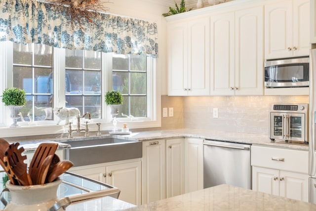 kitchen featuring decorative backsplash, stainless steel appliances, sink, light stone countertops, and white cabinetry