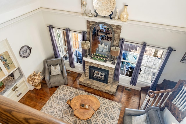 living room featuring dark wood-type flooring, a stone fireplace, and ornamental molding