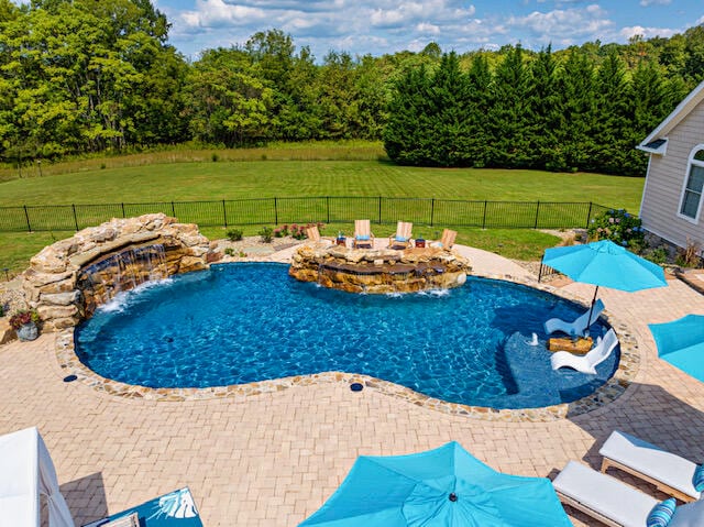 view of pool featuring a patio area, a hot tub, pool water feature, a lawn, and a fire pit