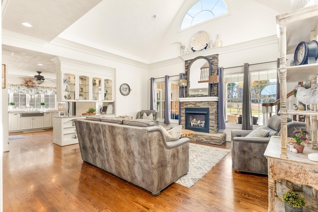 living room featuring a stone fireplace, hardwood / wood-style floors, crown molding, high vaulted ceiling, and ceiling fan