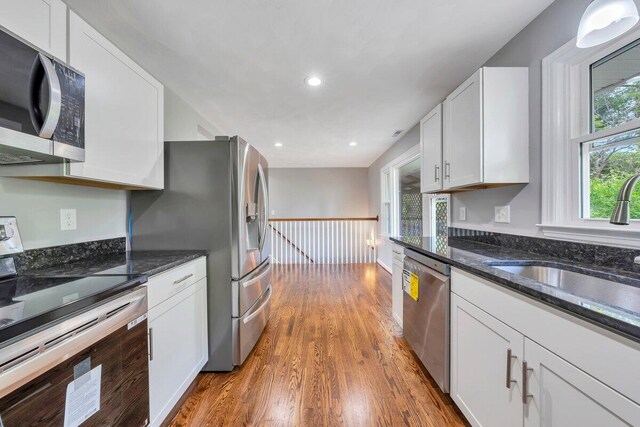 kitchen with wood finished floors, a sink, dark stone counters, stainless steel appliances, and white cabinetry