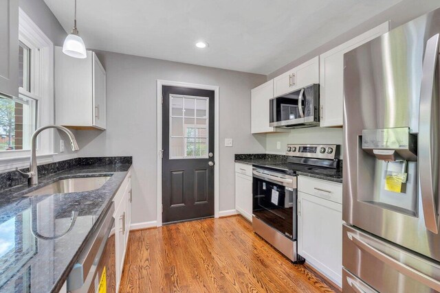 kitchen featuring white cabinets, appliances with stainless steel finishes, a sink, light wood finished floors, and dark stone counters