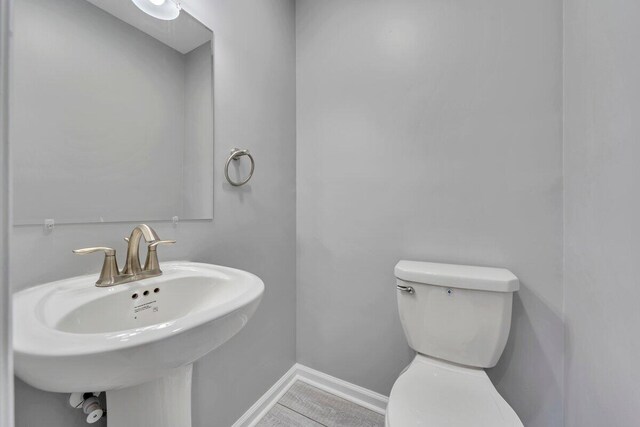half bath featuring toilet, baseboards, and a sink