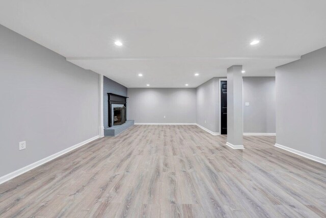 finished basement with baseboards, a brick fireplace, recessed lighting, and light wood-style flooring