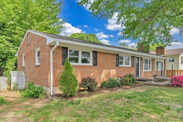 ranch-style house with brick siding, a chimney, fence, and a front yard