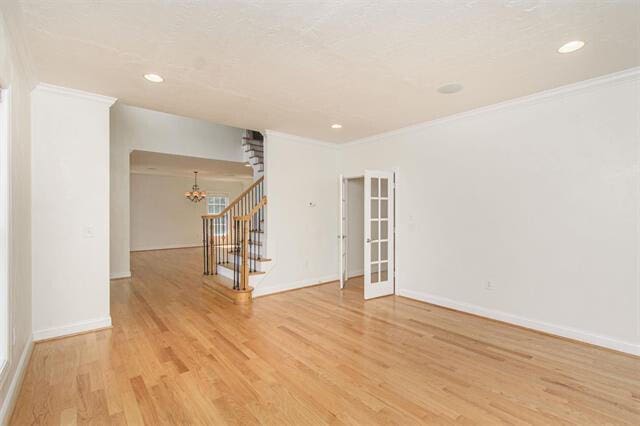 spare room featuring a notable chandelier, ornamental molding, and light wood-type flooring