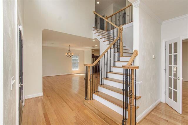 stairway with ornamental molding, hardwood / wood-style floors, and a chandelier