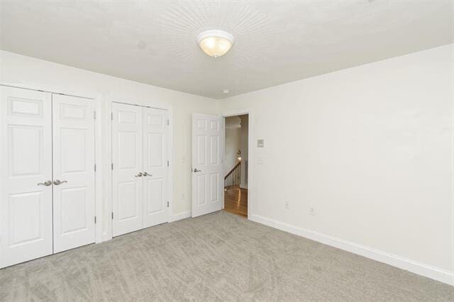 unfurnished bedroom with multiple closets and light carpet