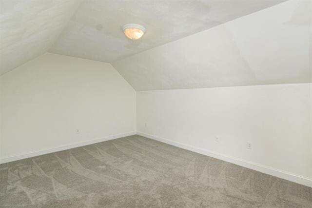 additional living space featuring light colored carpet and vaulted ceiling