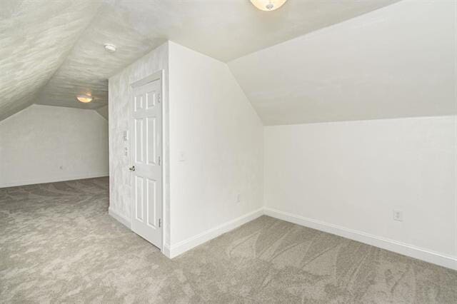 bonus room with lofted ceiling and light colored carpet