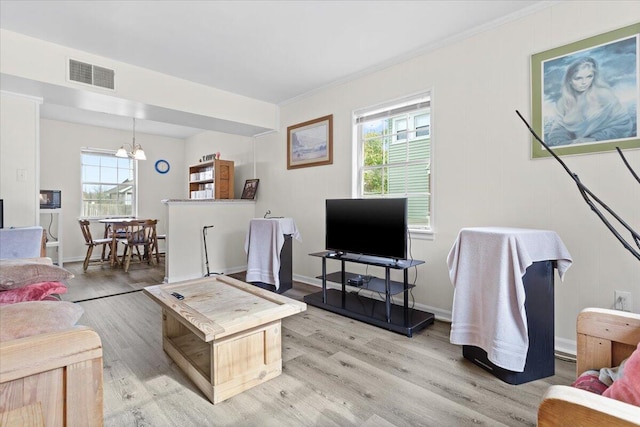 living room with light wood-type flooring, a notable chandelier, ornamental molding, and plenty of natural light