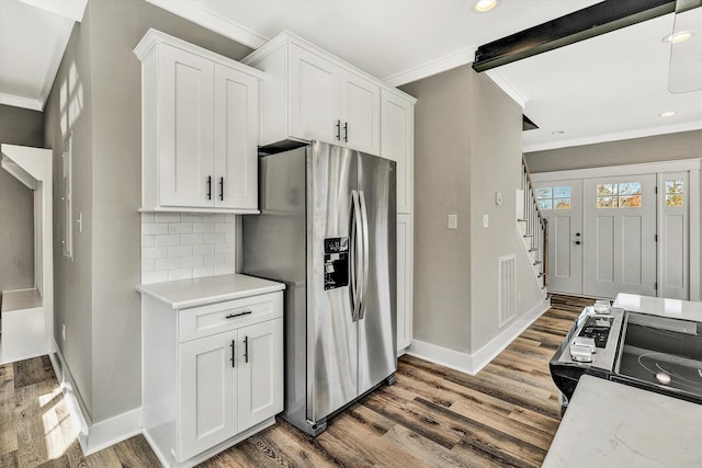 kitchen with dark wood-type flooring, white cabinets, tasteful backsplash, ornamental molding, and appliances with stainless steel finishes