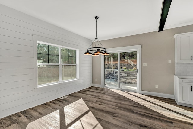 unfurnished dining area featuring plenty of natural light, dark wood-type flooring, beamed ceiling, and a chandelier