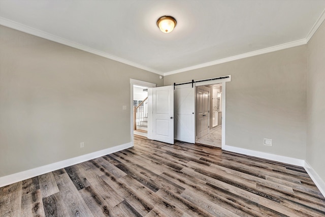 unfurnished bedroom with ensuite bath, wood-type flooring, a barn door, and crown molding