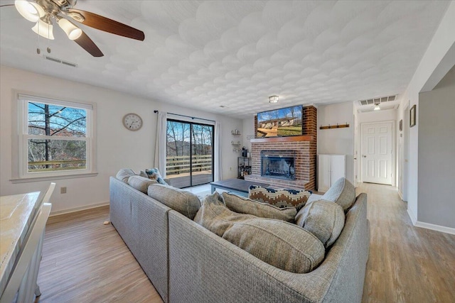 living room featuring a fireplace, light hardwood / wood-style floors, a wealth of natural light, and ceiling fan