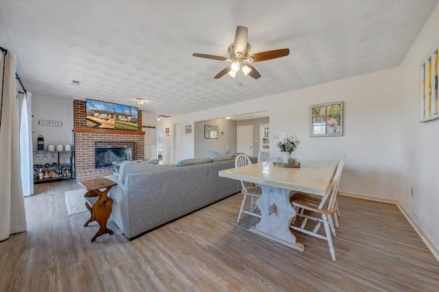 living room featuring ceiling fan, hardwood / wood-style floors, and a brick fireplace