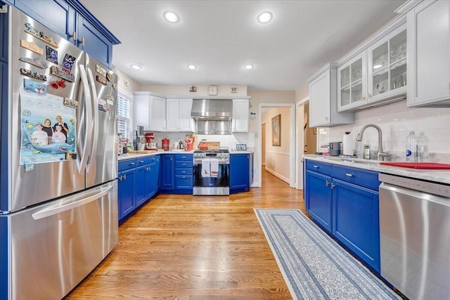 kitchen with white cabinetry, blue cabinets, appliances with stainless steel finishes, and wall chimney range hood