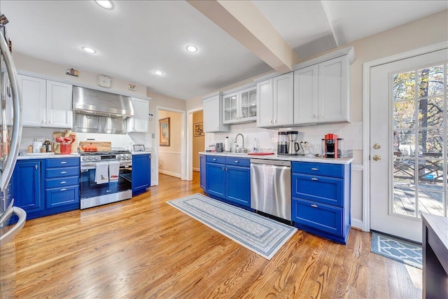 kitchen with white cabinets, wall chimney exhaust hood, blue cabinets, and appliances with stainless steel finishes