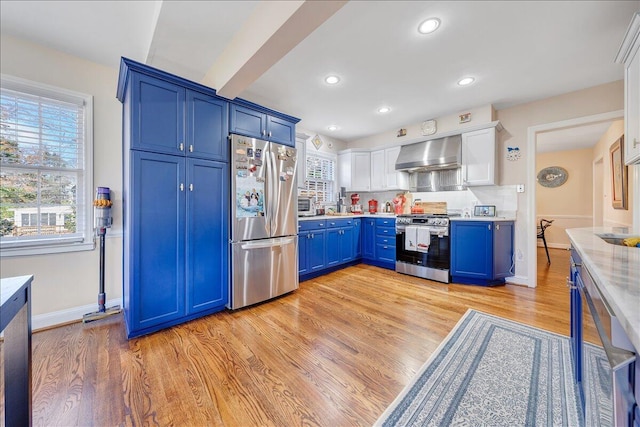 kitchen featuring blue cabinets, exhaust hood, appliances with stainless steel finishes, and light hardwood / wood-style flooring