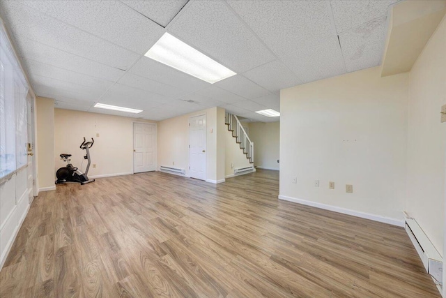 basement with a drop ceiling, wood-type flooring, and baseboard heating