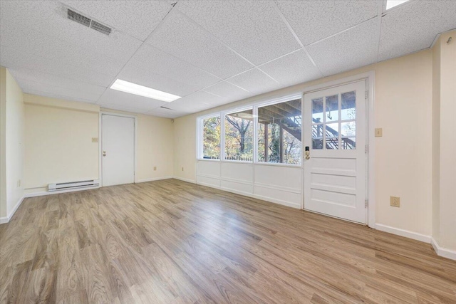 interior space featuring a drop ceiling, light hardwood / wood-style floors, and a baseboard heating unit