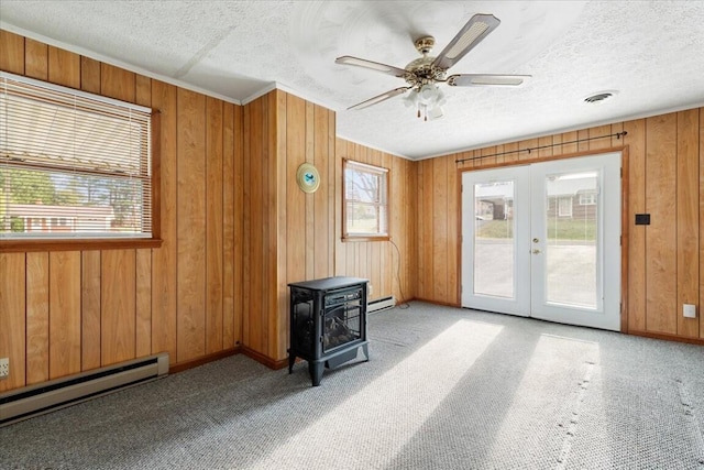 interior space with a wood stove, wooden walls, french doors, and a baseboard heating unit