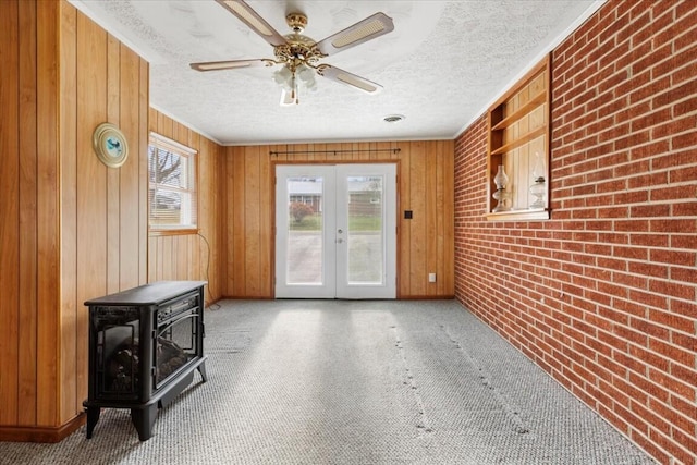 interior space with french doors, a textured ceiling, ceiling fan, a wood stove, and wood walls