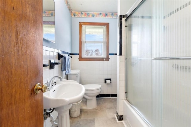 bathroom featuring tile patterned flooring, toilet, tile walls, and bath / shower combo with glass door