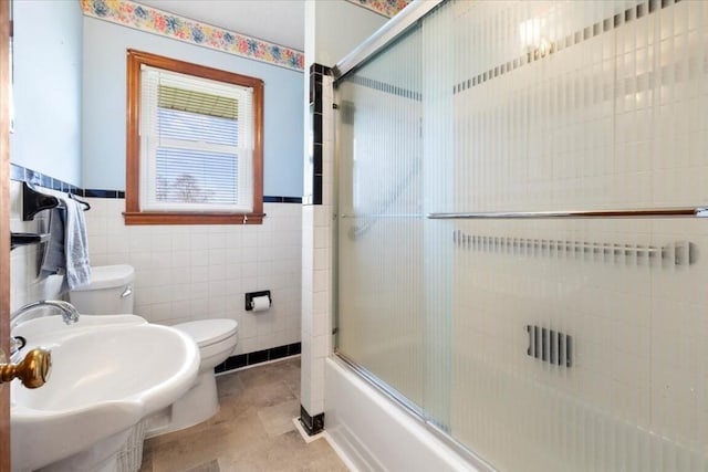 full bathroom featuring tile patterned flooring, toilet, bath / shower combo with glass door, and tile walls