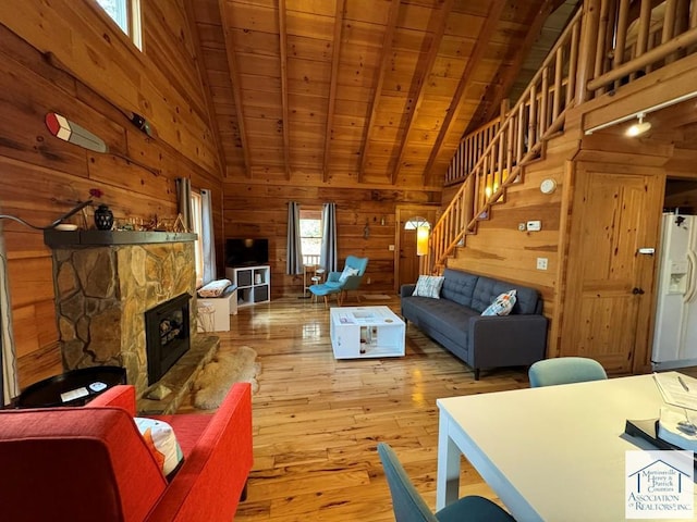 living room with wood walls, wooden ceiling, a stone fireplace, light hardwood / wood-style flooring, and lofted ceiling with beams