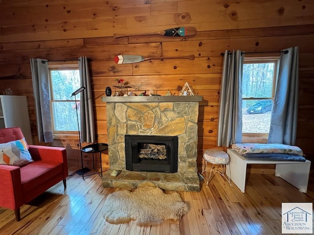 living area featuring a stone fireplace, wooden walls, and wood-type flooring