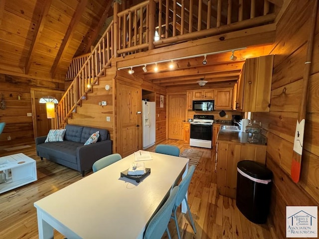 dining space featuring track lighting, light hardwood / wood-style floors, wood walls, and vaulted ceiling with beams