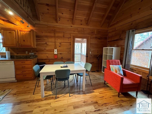 dining area with light wood-type flooring, a healthy amount of sunlight, and vaulted ceiling with beams