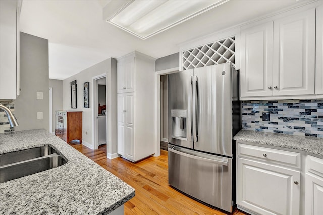 kitchen featuring light stone counters, stainless steel fridge, white cabinetry, sink, and light hardwood / wood-style flooring