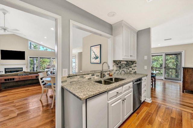 kitchen featuring white cabinets, sink, stainless steel dishwasher, light stone countertops, and light wood-type flooring