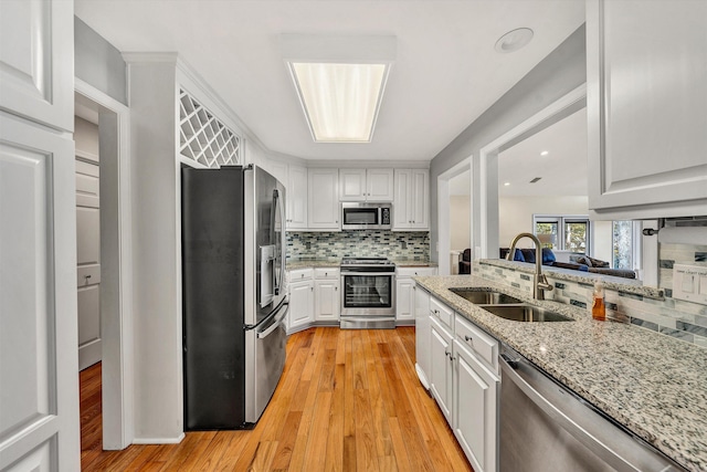 kitchen with light hardwood / wood-style floors, sink, tasteful backsplash, white cabinetry, and appliances with stainless steel finishes