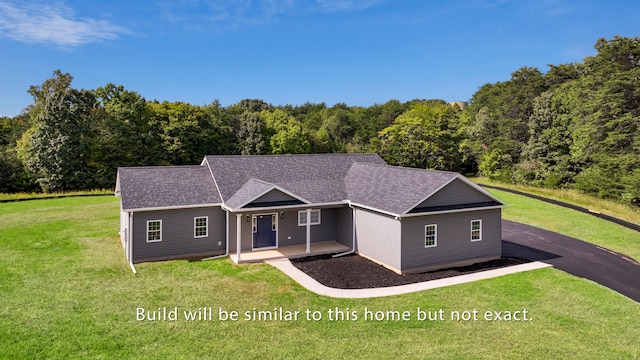 ranch-style home with covered porch, a front lawn, a shingled roof, and a wooded view