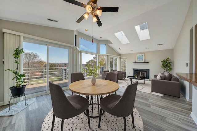 dining room featuring a glass covered fireplace, a skylight, light wood-type flooring, visible vents, and ceiling fan