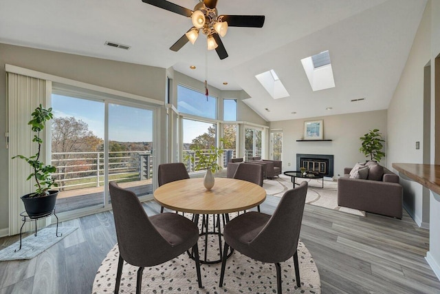 dining area featuring visible vents, a ceiling fan, a glass covered fireplace, light wood-style floors, and high vaulted ceiling