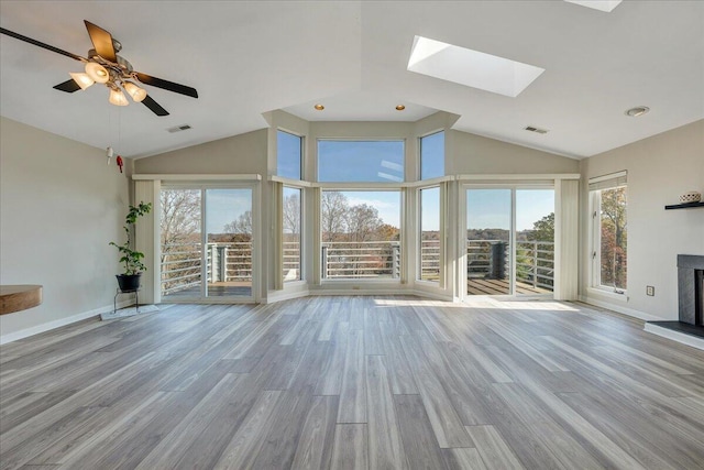 unfurnished living room featuring ceiling fan, a skylight, light hardwood / wood-style flooring, and a wealth of natural light