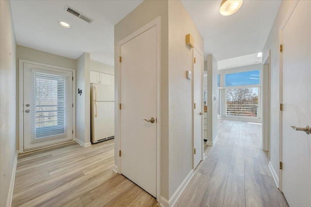 hallway featuring baseboards, visible vents, and light wood finished floors