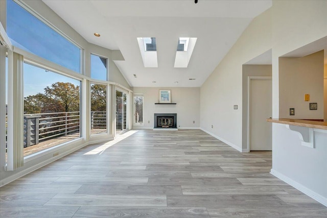 unfurnished living room featuring light wood-style floors, a skylight, a glass covered fireplace, and baseboards